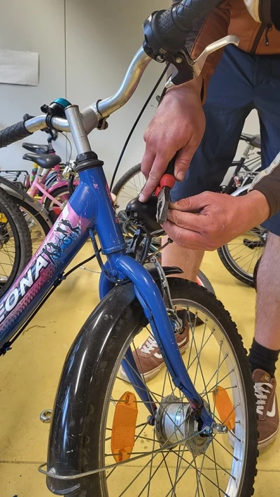 A person uses pliers to cut a brake cable on a blue children's bicy