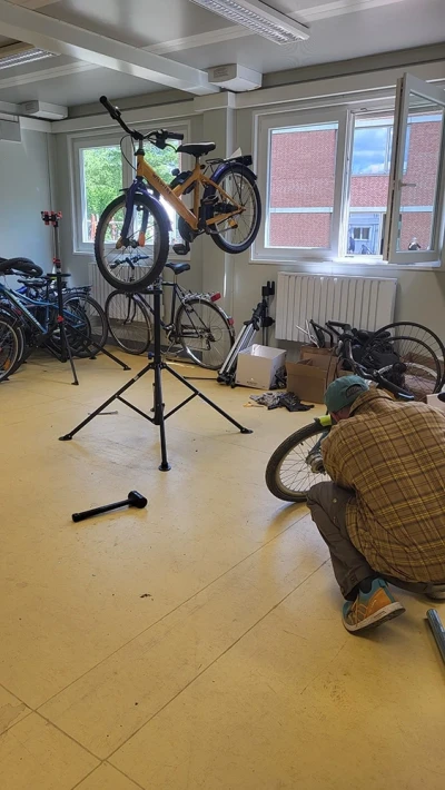 A person is kneeling on the floor, repairing the front wheel of a children's bicycle mounted on a repair stand.